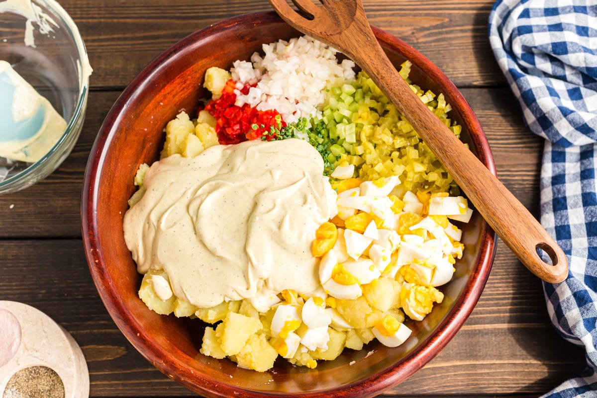 dressing on top of potato salad ingredients in bowl