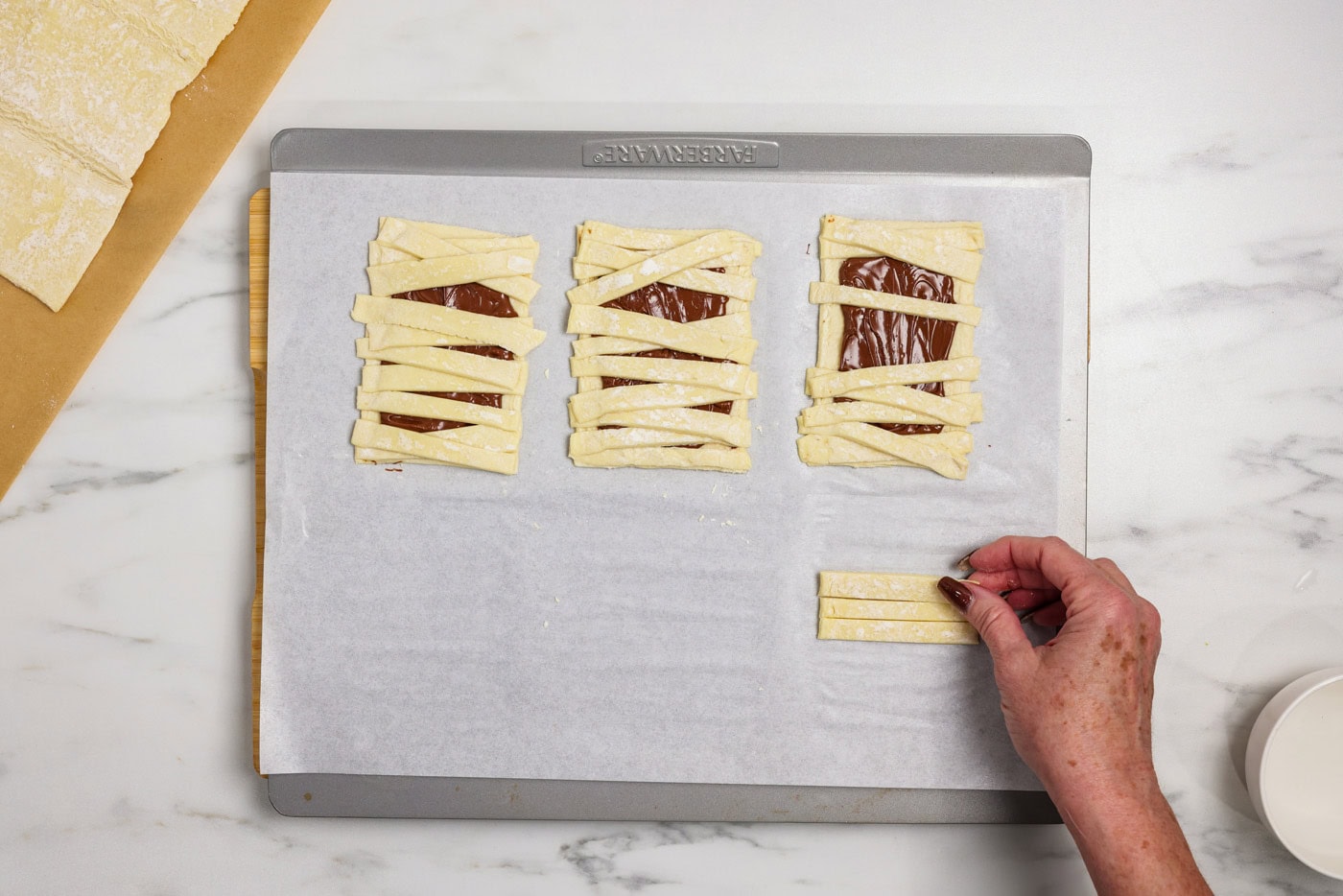 hand placing strips of puff pastry over nutella coated rectangle