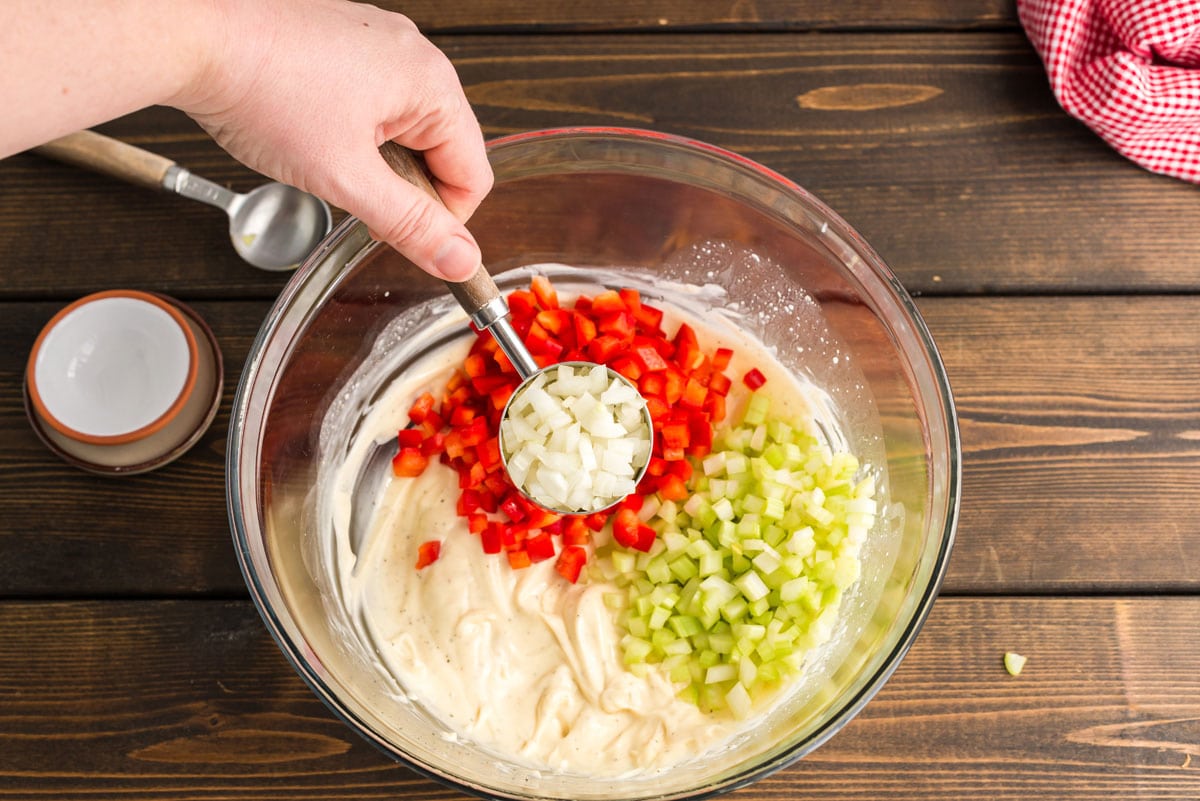 adding onion to dressing and vegetables in a bowl