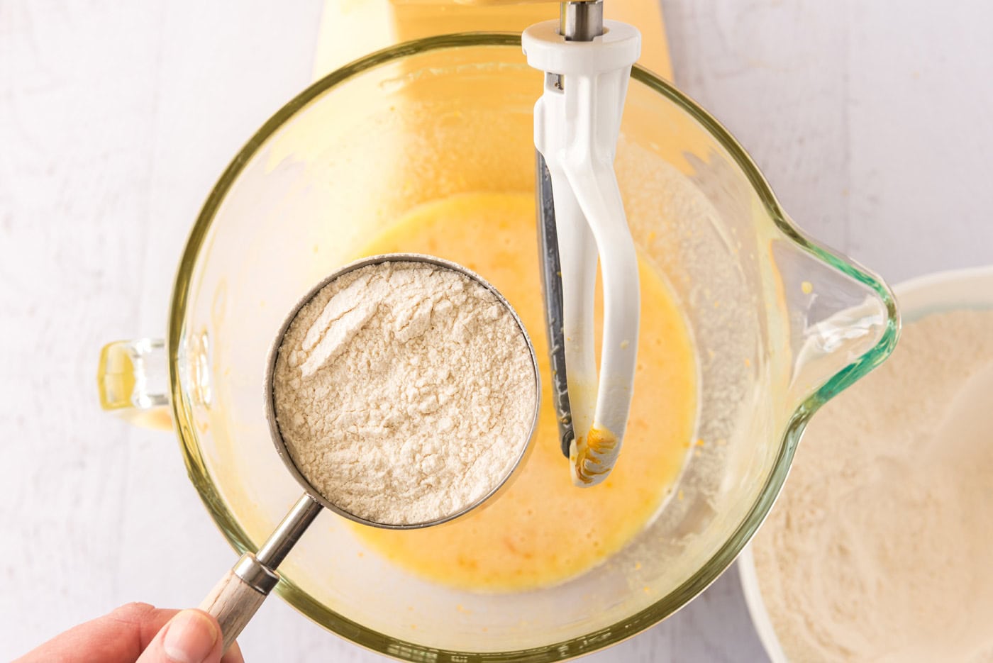 cup of flour over bowl of orange cupcake batter