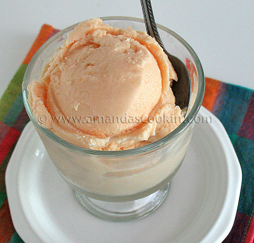 A close up photo of orange ice cream in a clear dish.
