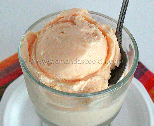 A close up photo of orange ice cream in a clear dish served with a spoon.