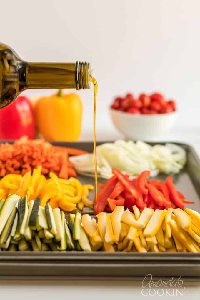 pouring olive oil onto fresh vegetables on a pan