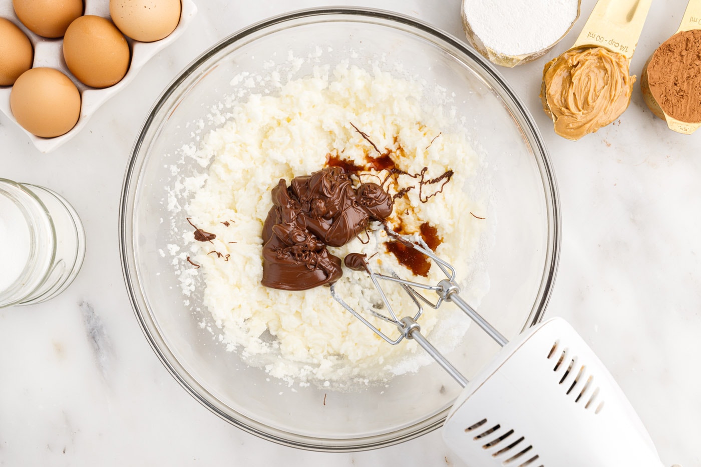 mixer combining melted chocolate and vanilla extract with butter and sugar mixture