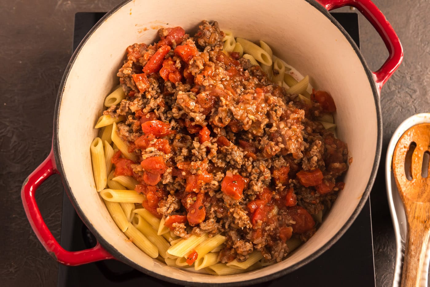 adding tomato and sausage sauce to pan with pasta
