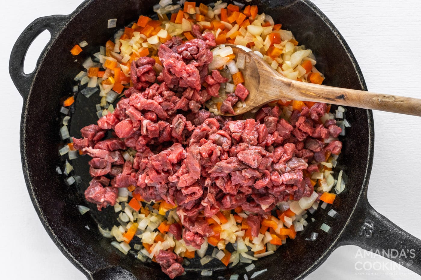 chopped steak on top of veggies in cast iron skillet