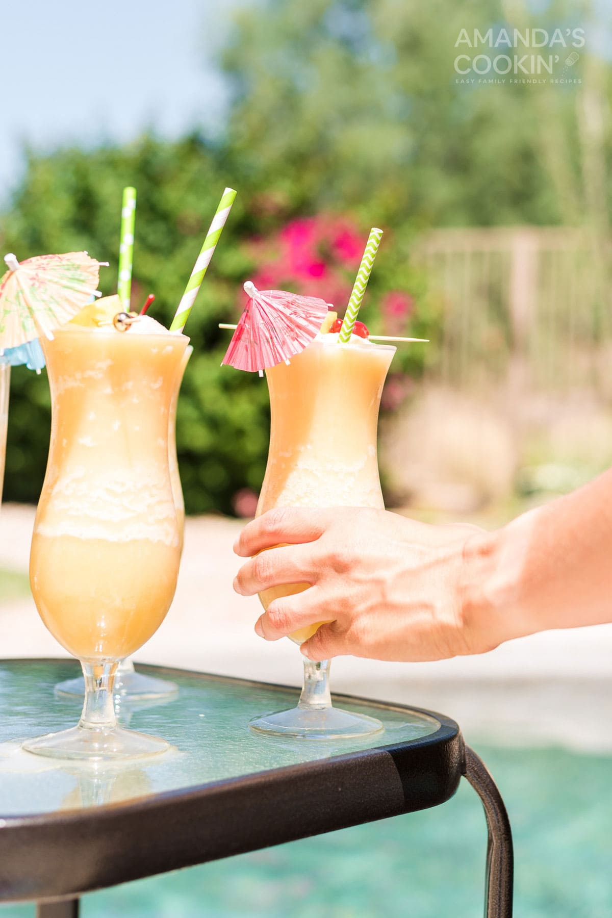 hand reaching for and picking up a pina colada cocktail by the pool