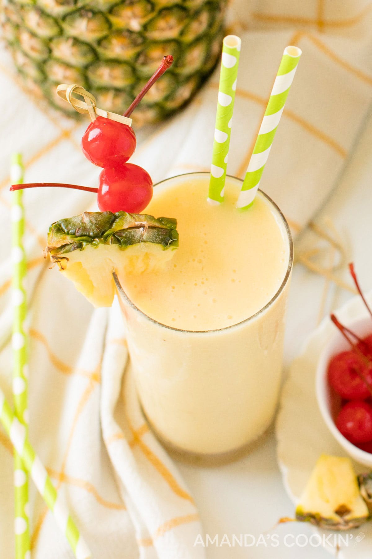 glass of rum slush with cherries and pineapple and green and white straws
