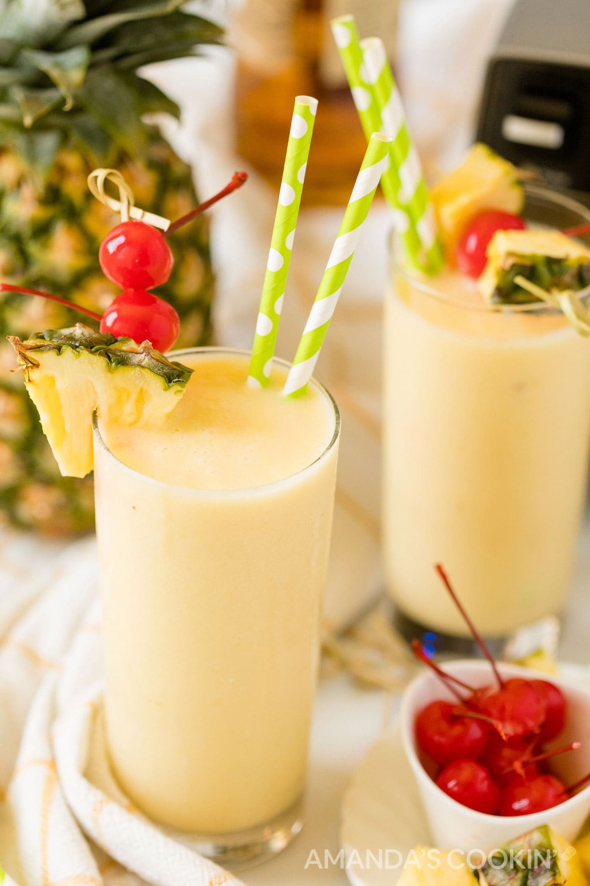 two glasses of pineapple rum slush with a blender in background