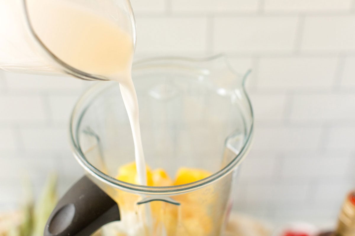 pouring coconut milk into blender with pineapple