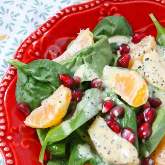A close up of a pomegranate clementine spinach salad on a red plate.