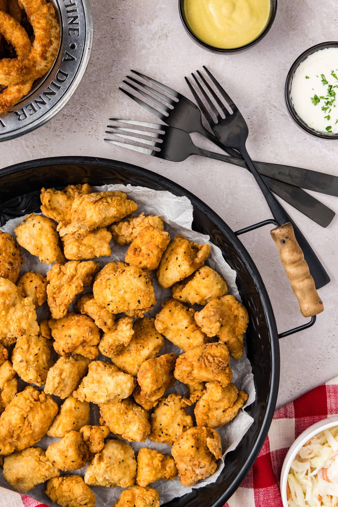 Tray of Popcorn Chicken with forks and dipping sauces on the side