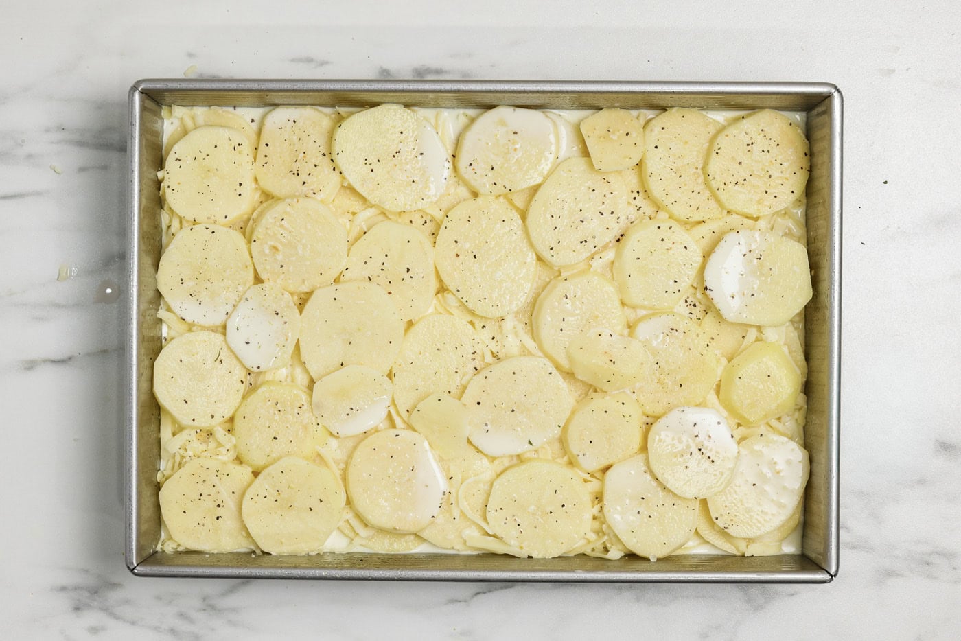 sliced potato layer on top of cream sauce and cheese in a baking pan