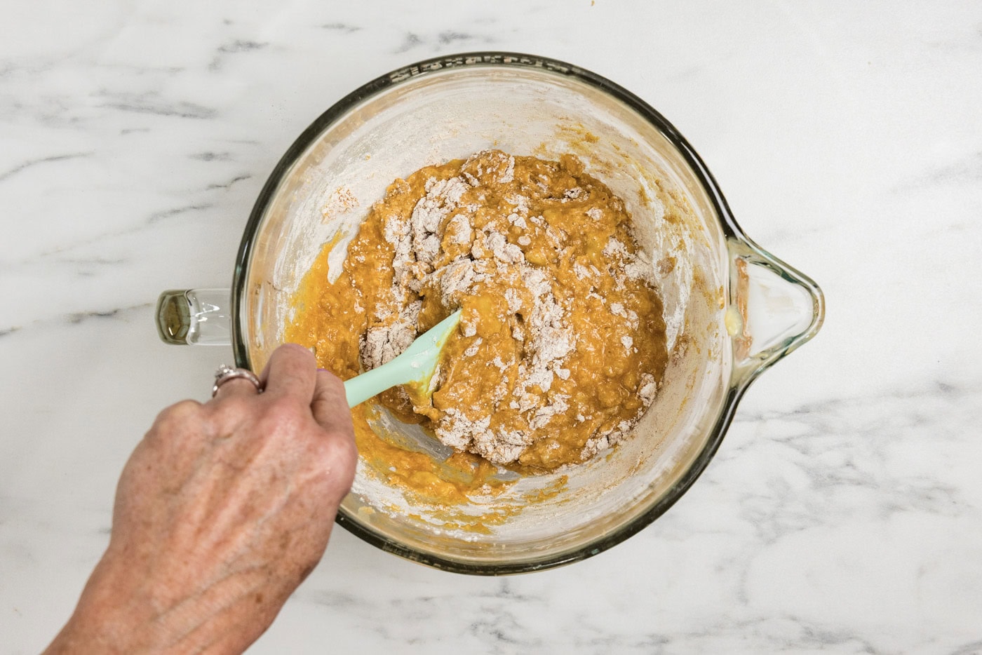 Hand using a rubber spatula to stir in dry ingredients into pumpkin mixture