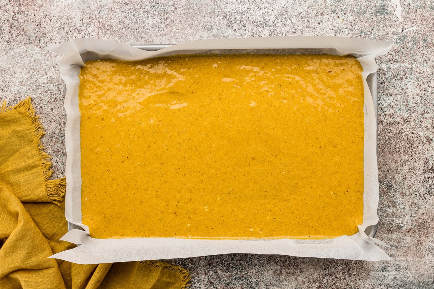 Pumpkin cake batter in a jelly roll pan lined with parchment paper