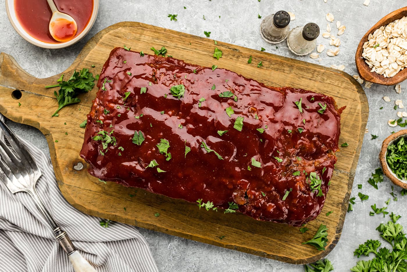 Overhead photo of glazed cooked Quaker Oats meatloaf on a cutting board with chopped parsley garnish