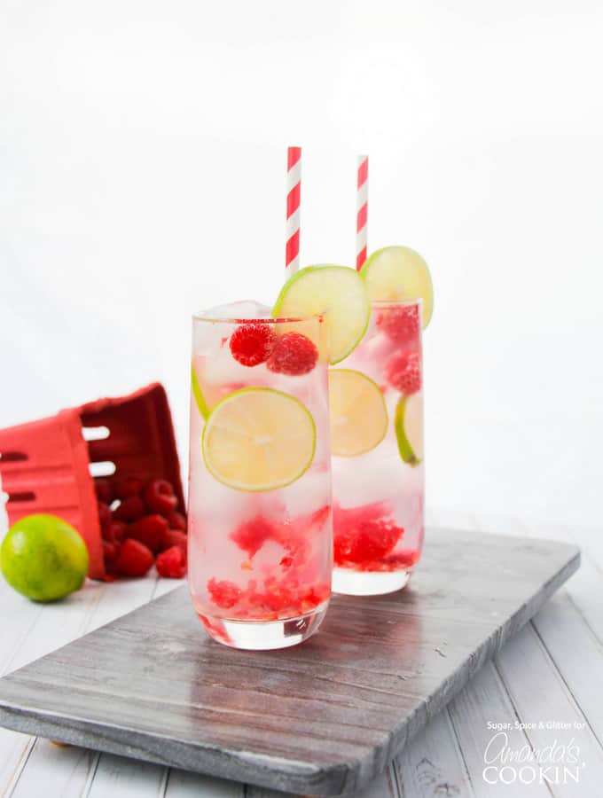 cocktail in glass with paper straws, lime, and raspberries