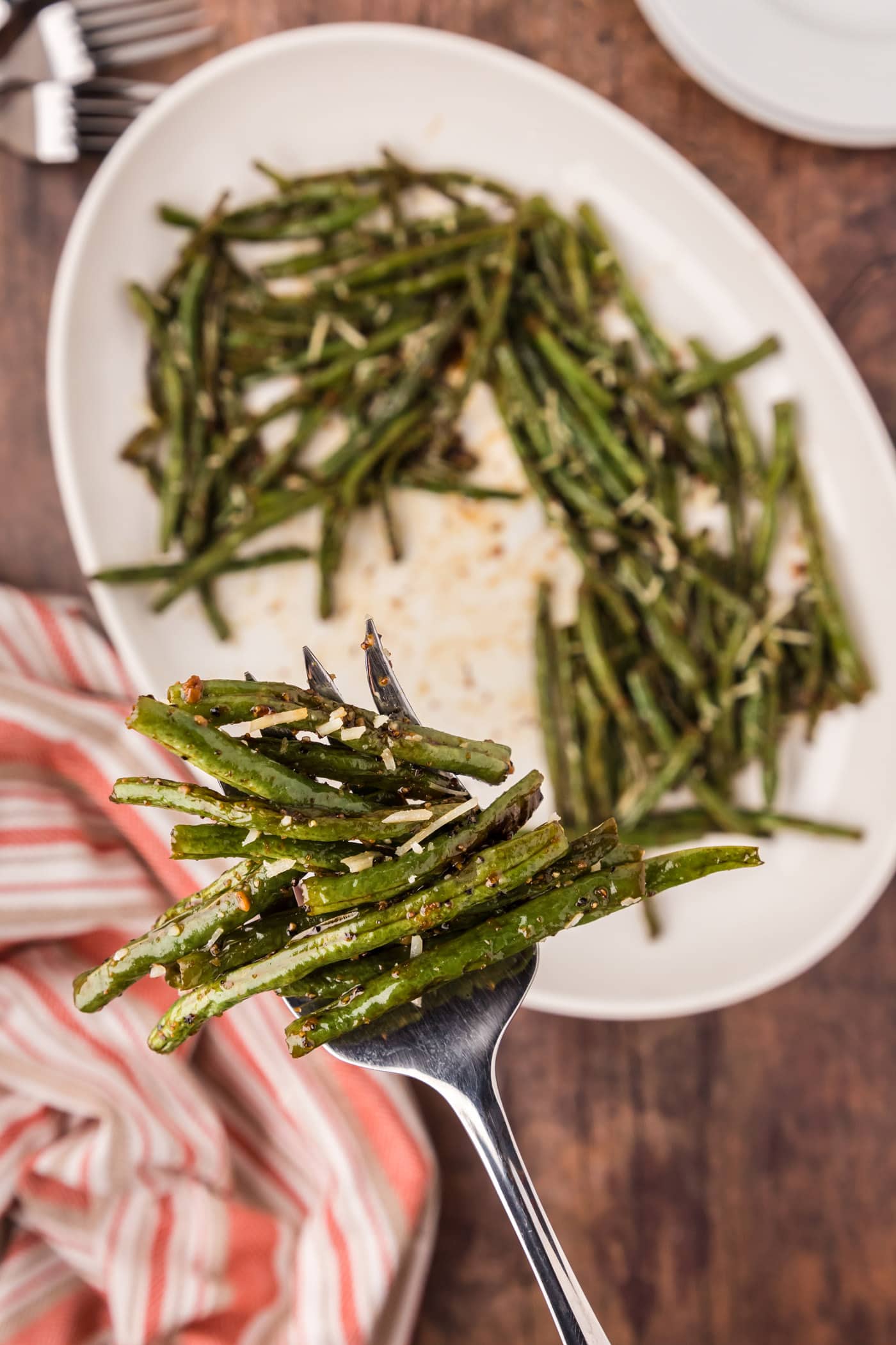 Serving fork full of Roasted Green Beans held above a platter of Roasted Green Beans