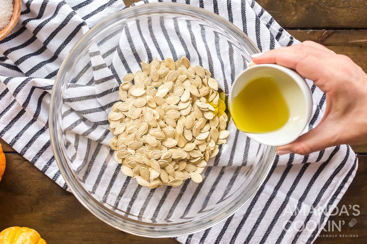 adding olive oil to pumpkin seeds in bowl