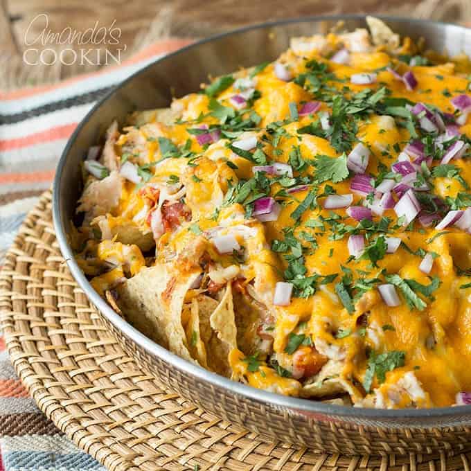 A bowl of loaded rotisserie chicken nachos resting on a wicker place mat.