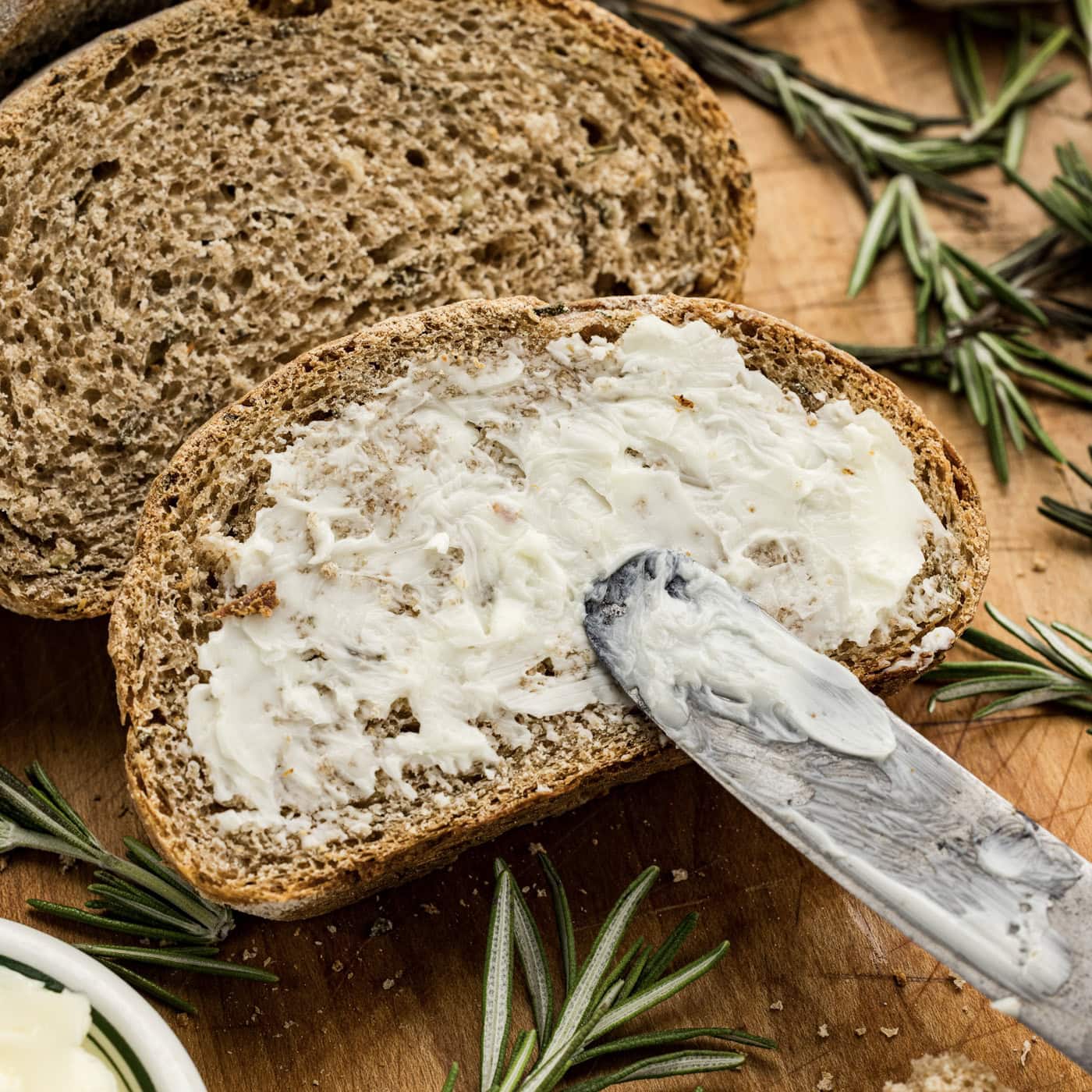 Knife spreading butter on a slice of Rosemary Garlic Bread