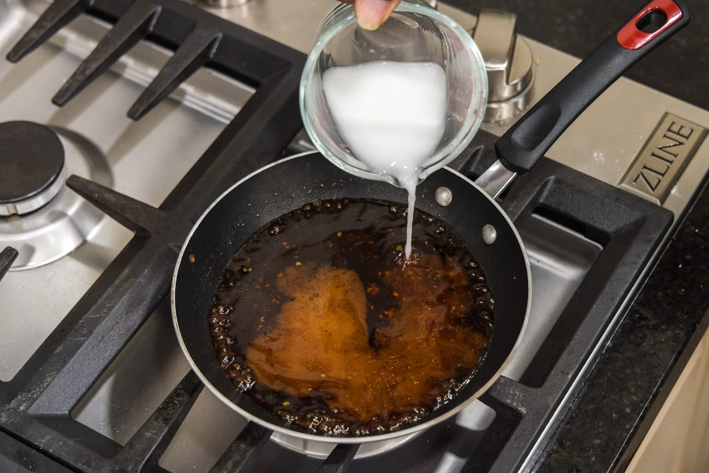 pouring cornstarch slurry into sauce in a skillet