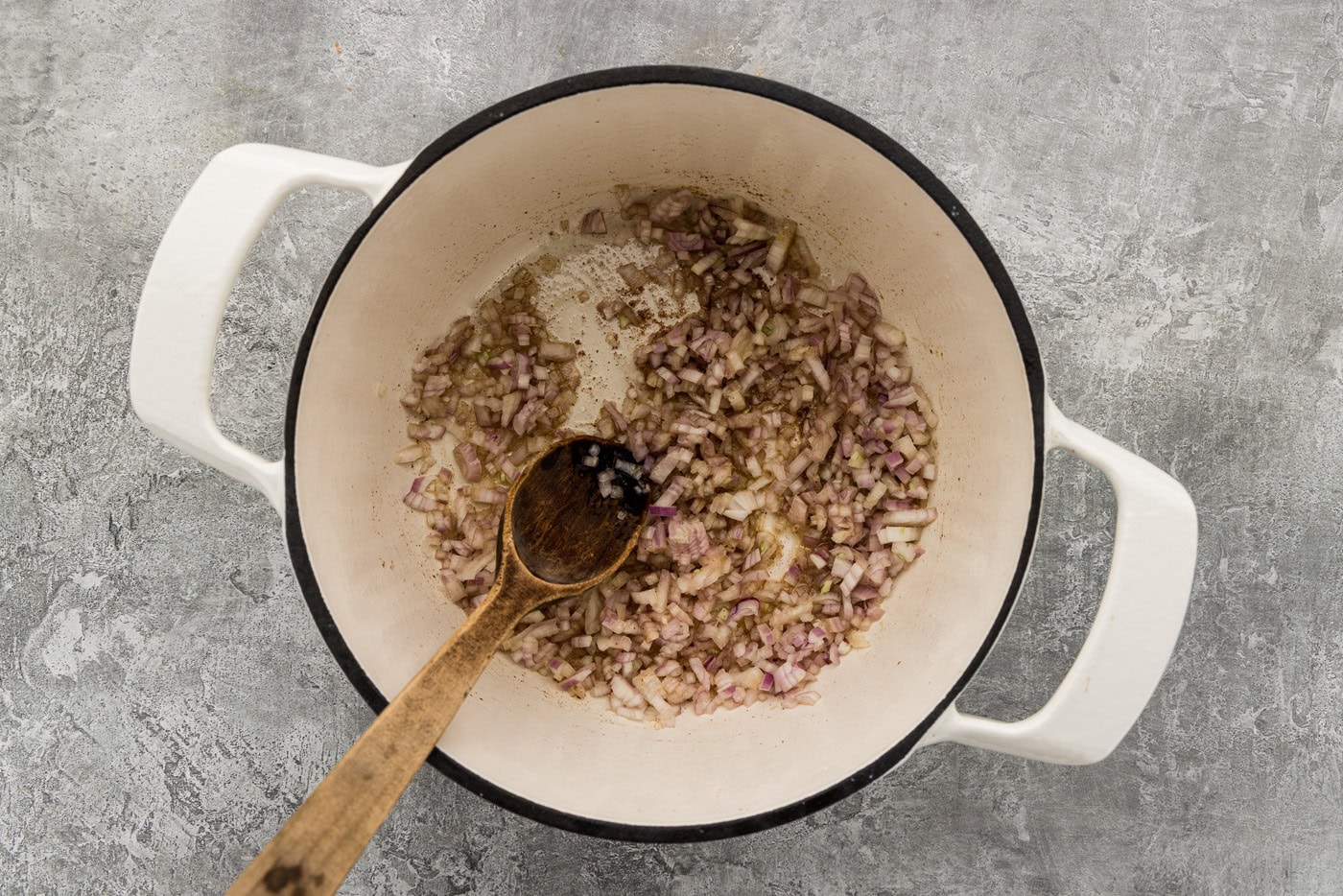 Chopped shallots sautéing in the Dutch oven with a wooden spoon