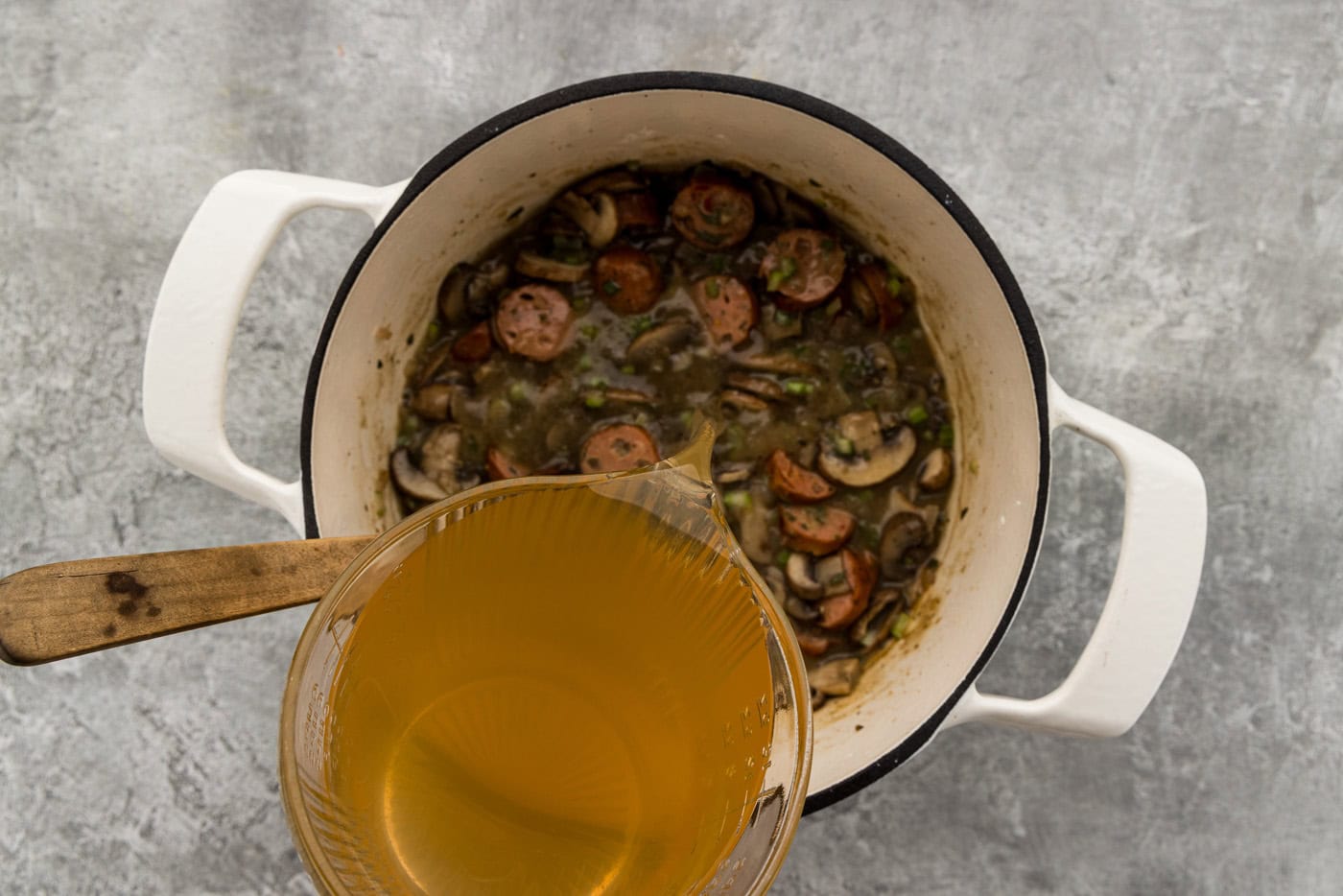 Pouring vegetable broth into the pot of sausage, mushrooms and celery