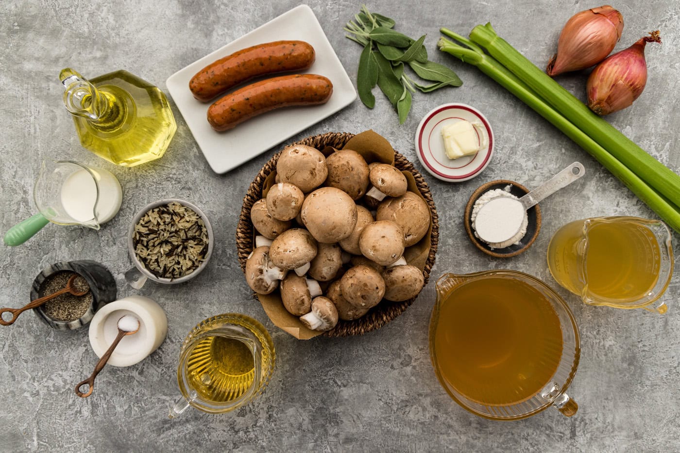 Ingredients for sausage mushroom wild rice soup including chicken sausage links, baby bella mushrooms, wild rice, shallots, celery, fresh sage, white wine and broth