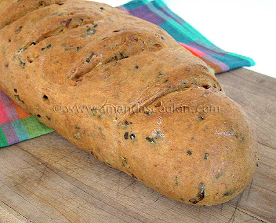 A close up photo of a loaf of scallion chive bread with garlic and rosemary on a wooden cutting board.
