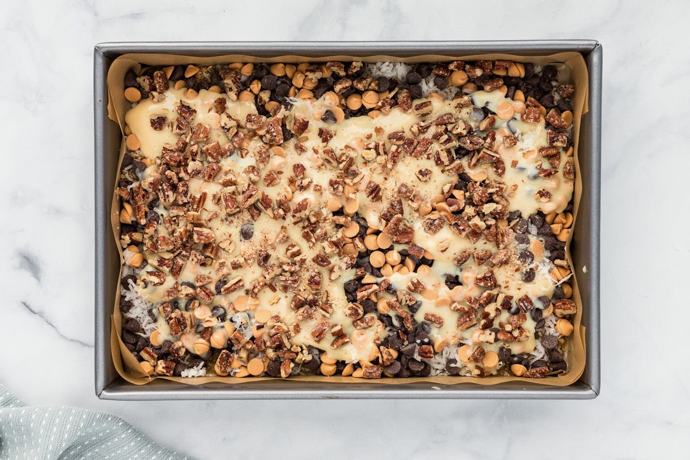 chopped pecans sprinkled over magic bars in a baking dish