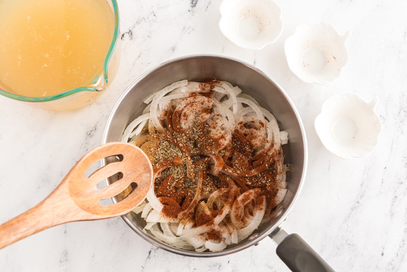sliced onion with chicken broth, spices, and seasonings in a saucepan