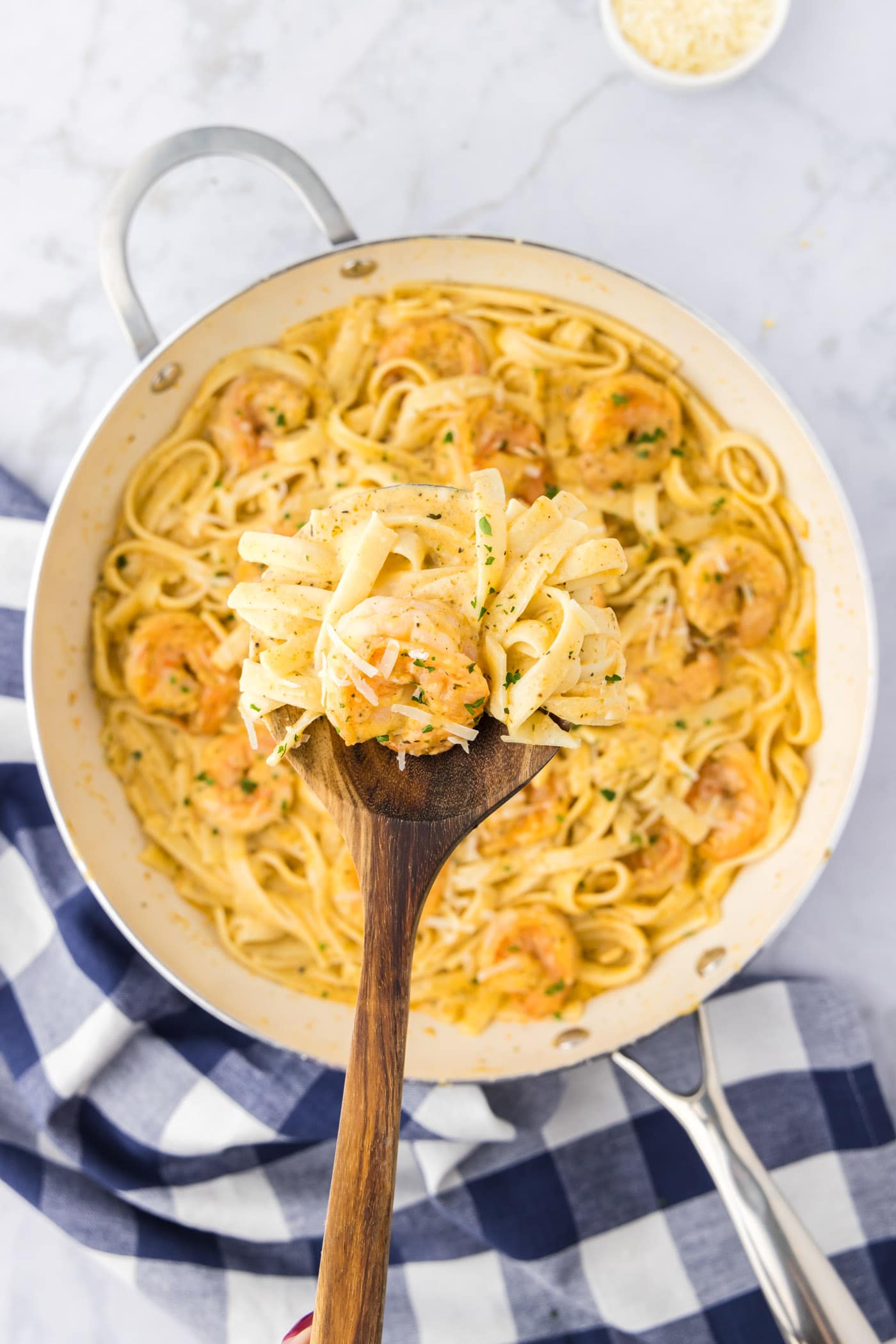 Spoonful of Shrimp Alfredo held above a skillet of Shrimp Alfredo