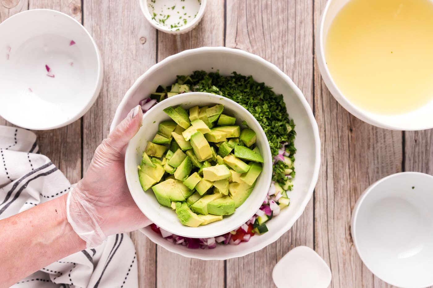 adding avocado to bowl of diced fruits and vegetables with shrimp