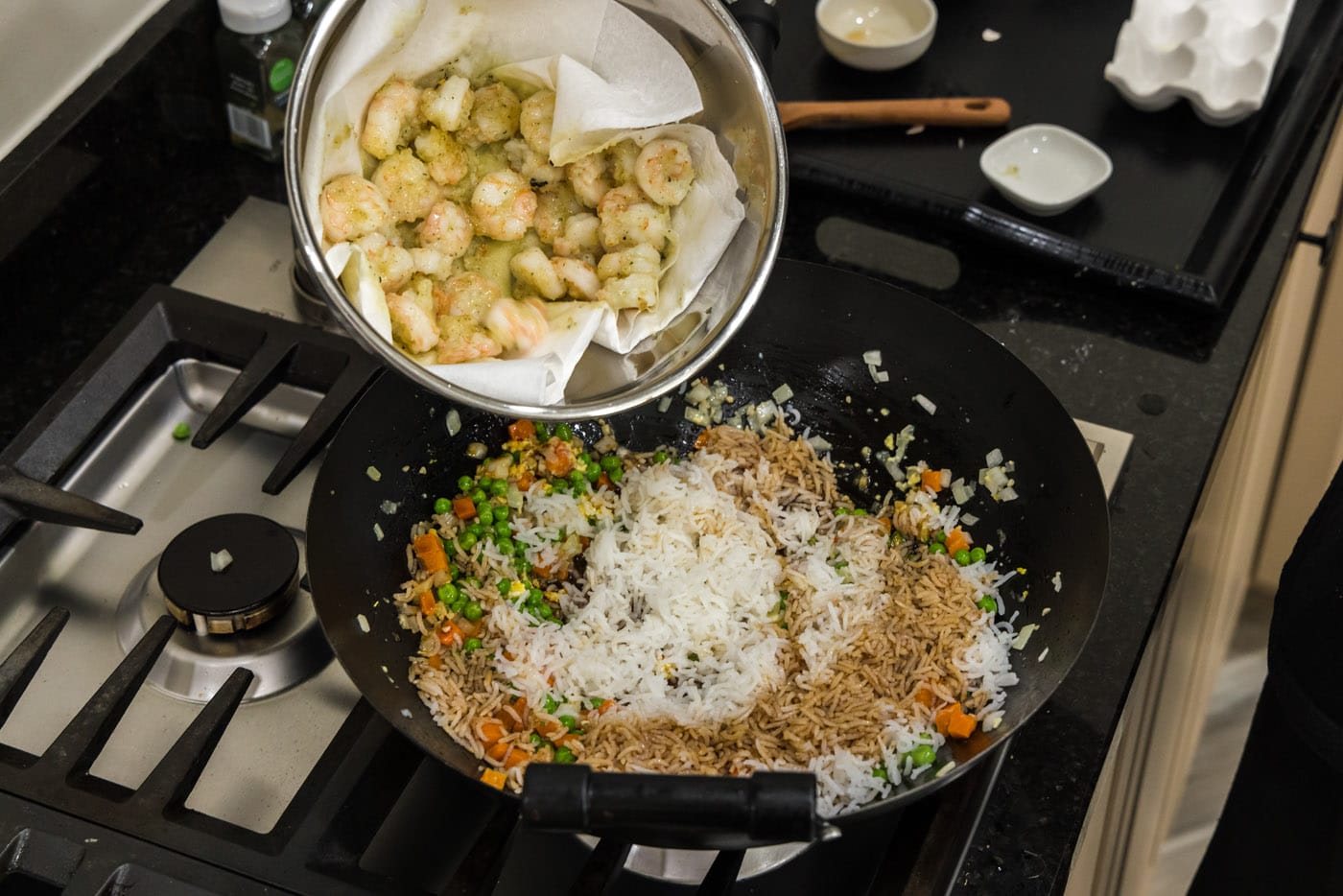adding cooked shrimp to wok with fried rice and vegetables