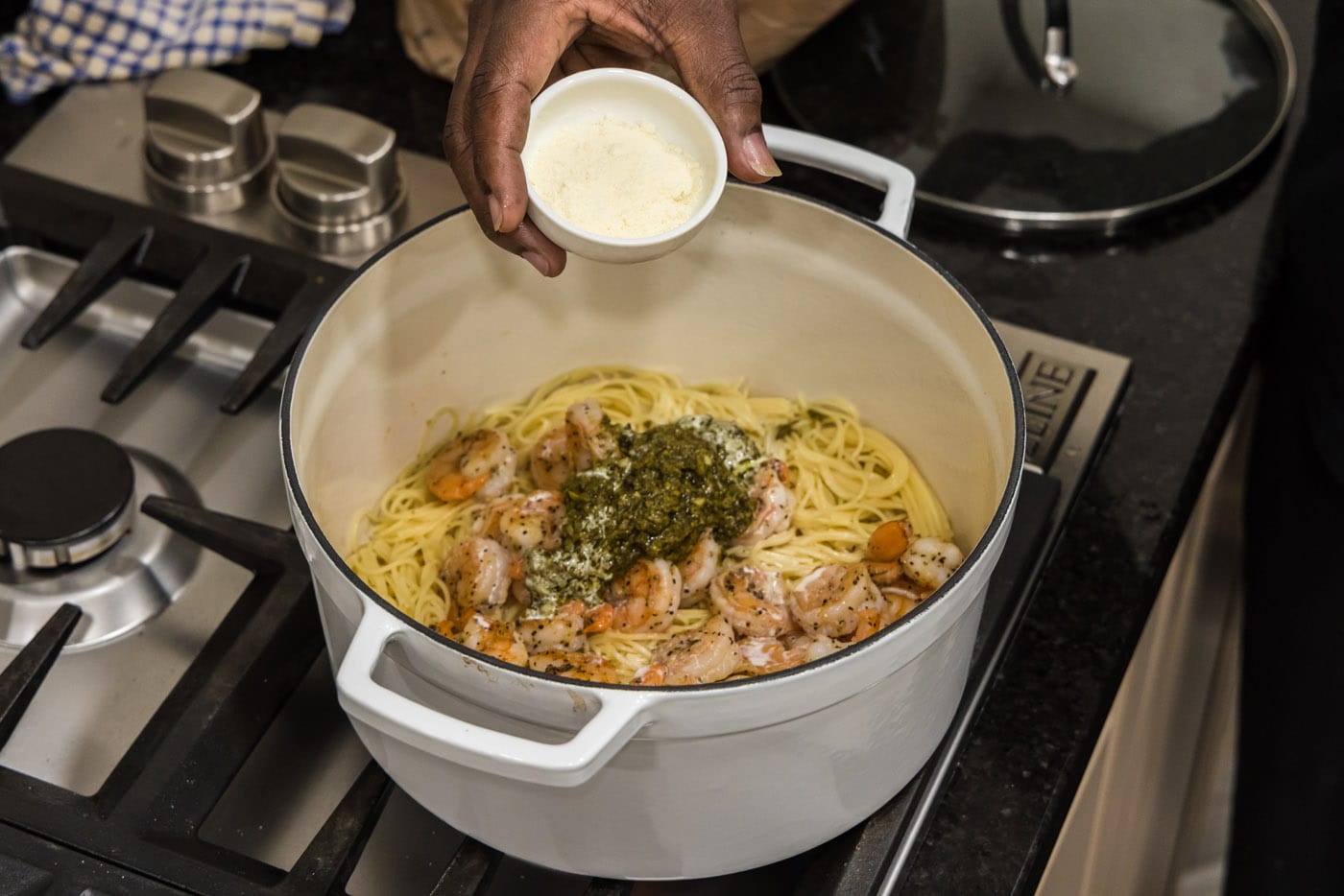pouring parmesan into pot with shrimp pesto pasta