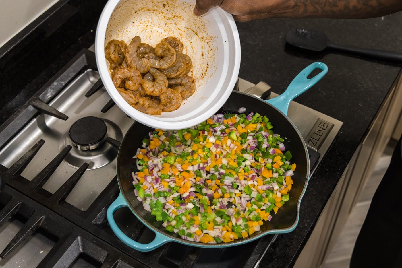 tossing seasoned shrimp into skillet with sauteed veggies