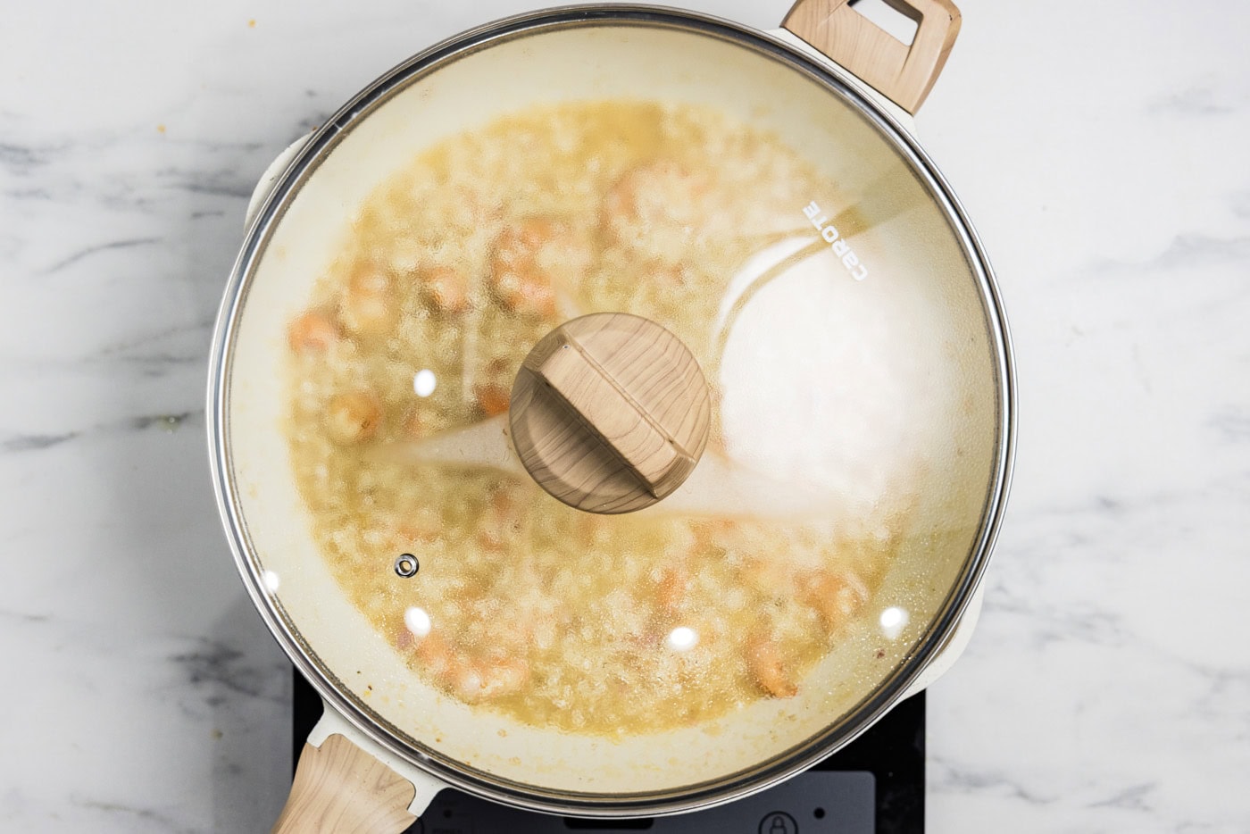 shrimp risotto in a skillet cooking with a lid