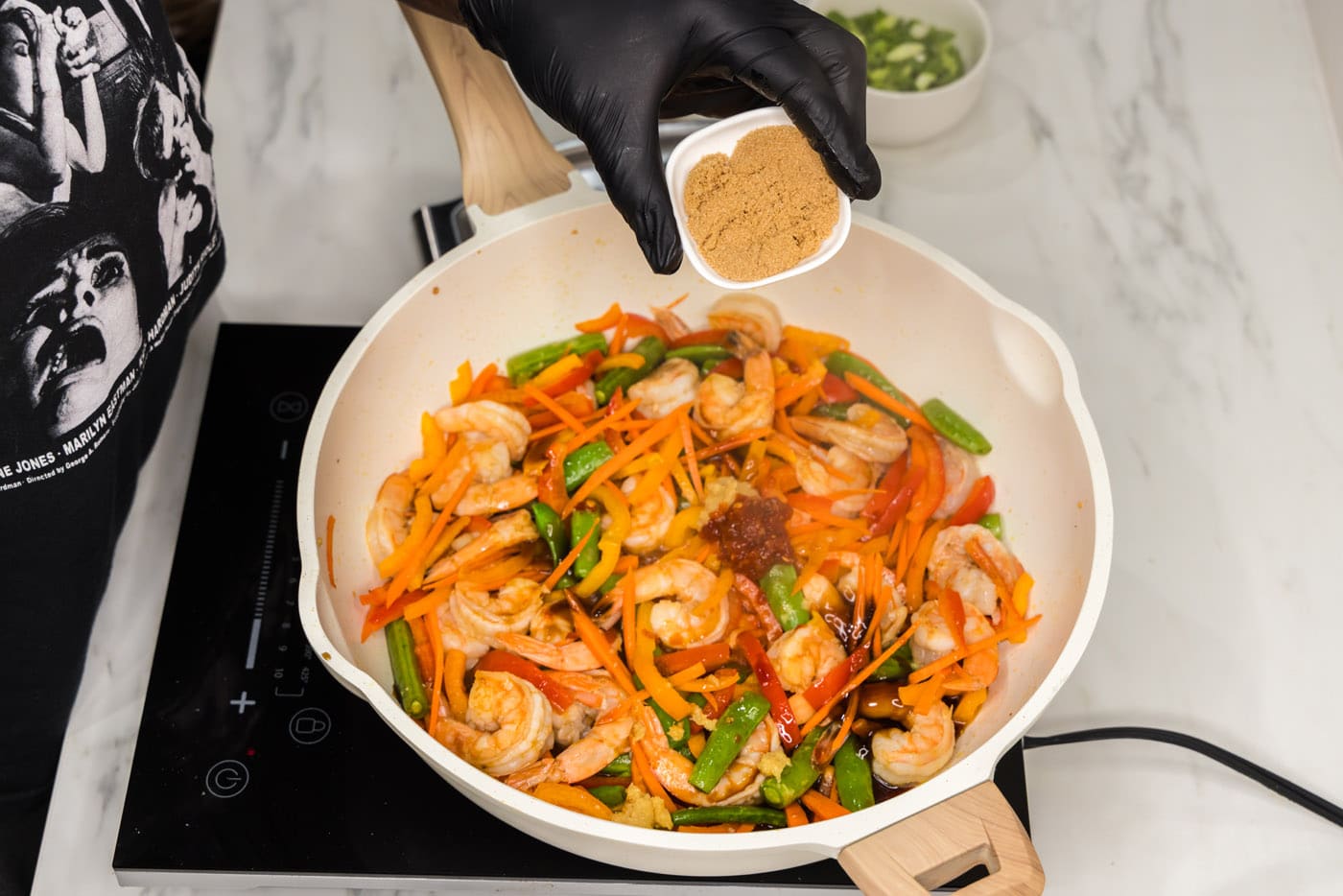 adding brown sugar to shrimp stir fry in a skillet