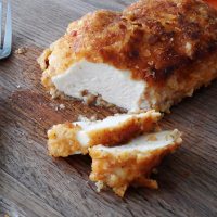A close up photo of a sliced oven fried chicken breast on a wooden cutting board.