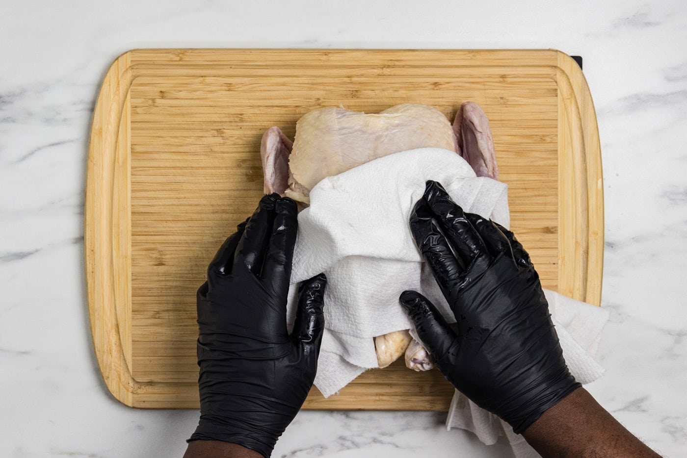 hands patting whole raw chicken dry with paper towels