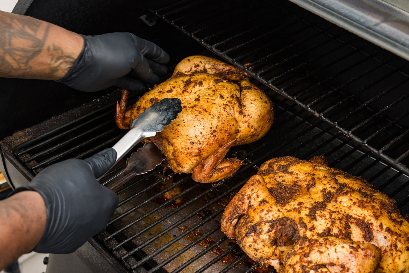 tongs flipping whole chicken upside down on a smoker grate