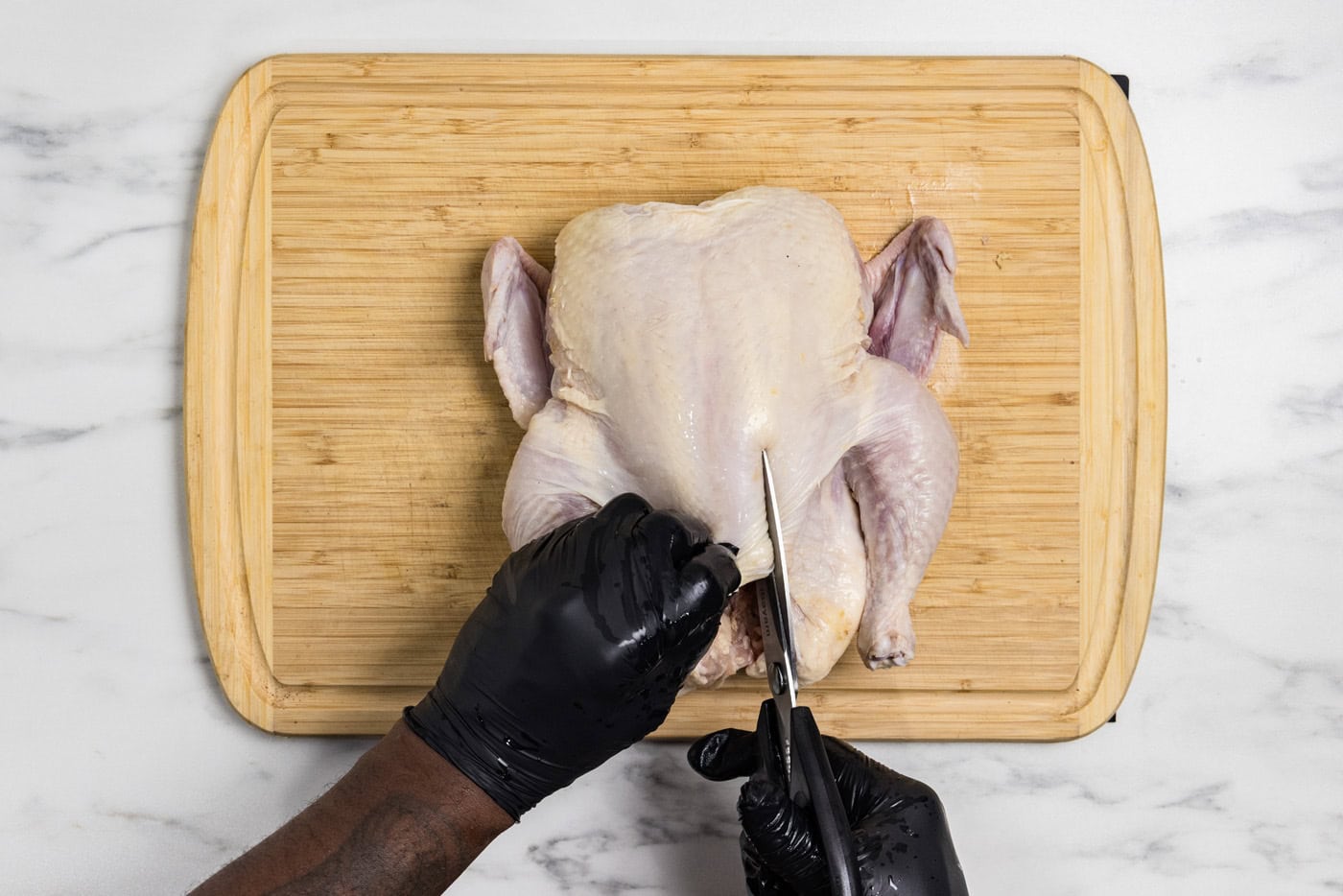 Using kitchen shears to cut along a whole raw chicken's back