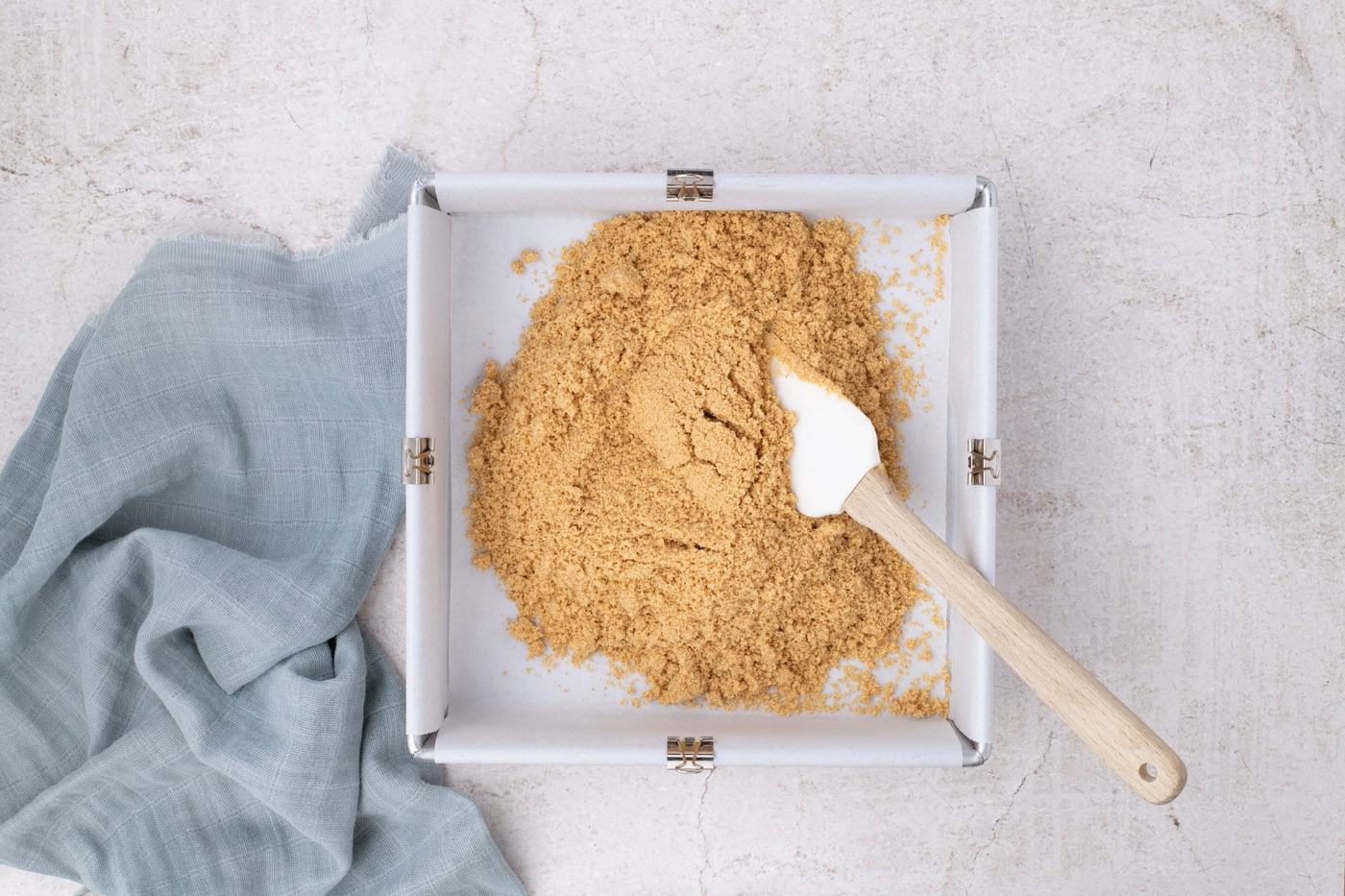 spreading graham cracker crust on bottom of a baking pa