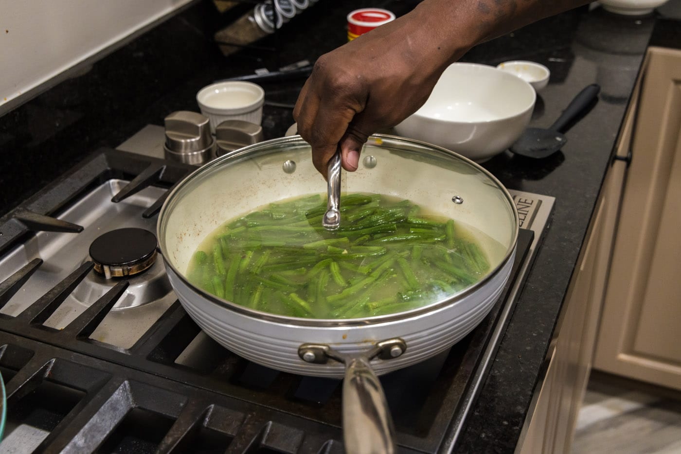 placing lid on skillet over green beans to cook