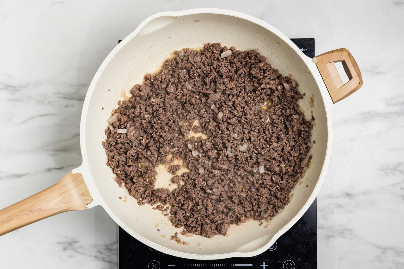 Ground beef browned with onion in a skillet, ready to be drained