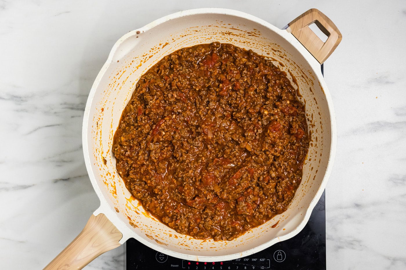 Thickened meat sauce simmering in a skillet for spaghetti pie