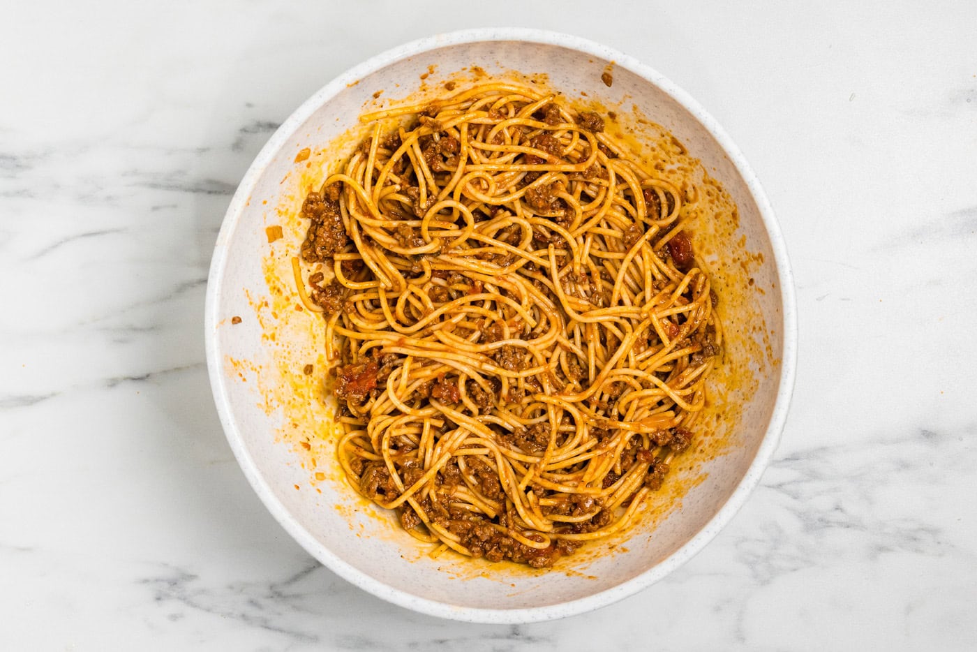 Cooked spaghetti combined with half of the meat sauce in a large mixing bowl