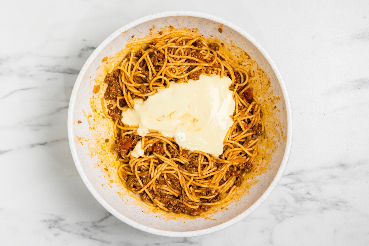 Whisked egg and ricotta mixture spooned over the spaghetti and meat sauce
