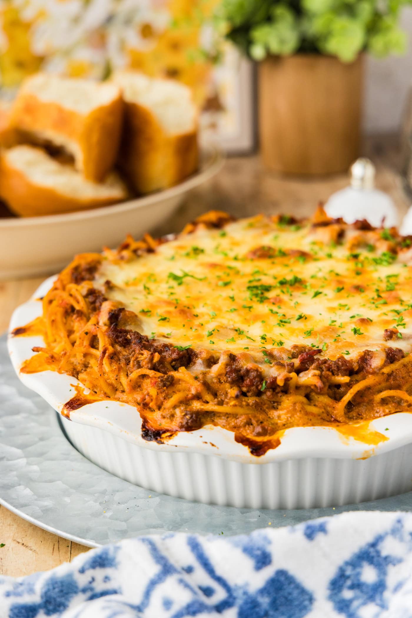 Baked spaghetti pie in a white deep dish pie plate on a galvanized tray with garlic bread